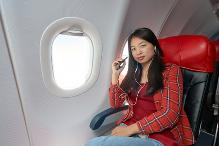 Young woman with smartphone inside of a single-aisle aircraft.
