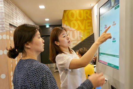 BUSAN, SOUTH KOREA - CIRCA MAY, 2017: women use ordering kiosk at McDonald's restaurant. McDonald's is an American hamburger and fast food restaurant chain.のeditorial素材