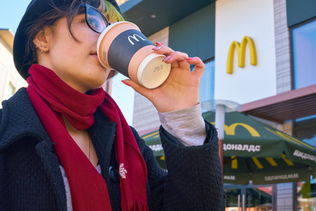KALININGRAD, RUSSIA - CIRCA APRIL, 2018: young woman drinks a coffee in the background of the McDonald's restaurant.のeditorial素材