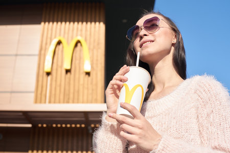 KALININGRAD, RUSSIA - OCTOBER 13, 2018: young woman drinks Coca-Cola in the background of the McDonald's restaurantのeditorial素材