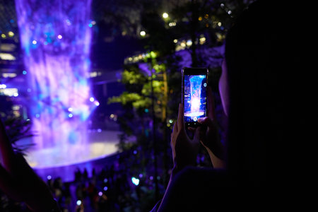 SINGAPORE - CIRCA APRIL, 2019: woman taking video of 40-meter HSBC Rain Vortex, the worldâs tallest indoor waterfall at the Jewel Changi Airport at night.のeditorial素材