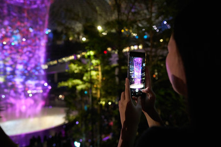 SINGAPORE - CIRCA APRIL, 2019: woman taking video of 40-meter HSBC Rain Vortex, the worldâs tallest indoor waterfall at the Jewel Changi Airport at night.のeditorial素材