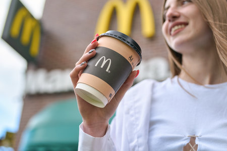 KALININGRAD, RUSSIA - CIRCA JULY, 2022: outdoor portrait of smiling woman with paper cup against the background of McDonald's restaurant, closed after sanctions were imposed.のeditorial素材
