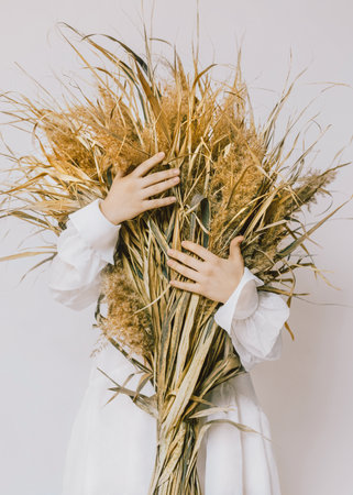 Loving nature Conceptual photo in minimal style Girl in white vintage dress is hugging large bouquet of dry plantsの写真素材