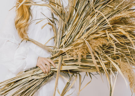 Dry flowers Close up photo in minimal style Girl in white vintage dress is holding big bouquet of fields plants in her handsの写真素材