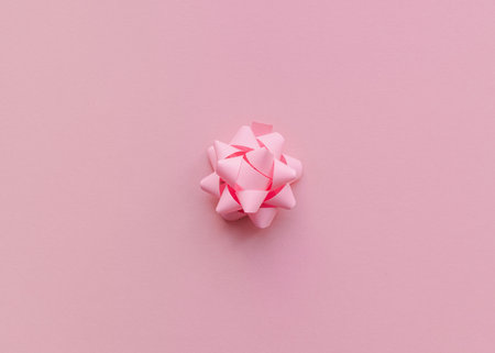 Decorative bow Close up photo in minimal style Pink paper gift bow on pink background Template for posters and bannersの写真素材