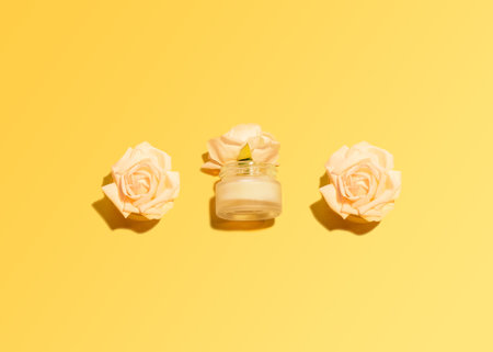Natural cosmetic Facial cream Top view photo Rose buds and glass jar with cream on bright yellow backgroundの写真素材