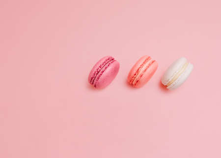 French biscuits Top view photo in minimal style White, pink and orange macaroons on pink backdrop...