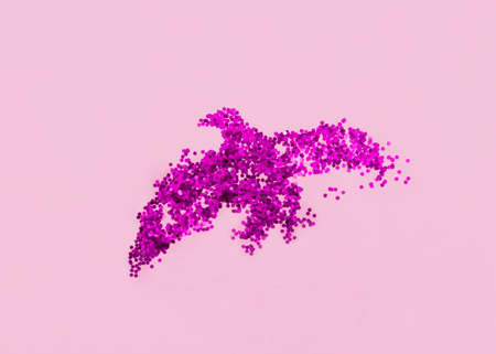 Shiny decorative bird. Top view photo for posters and banners. Glowing purple sparkles in birdie shape on pink backgroundの写真素材
