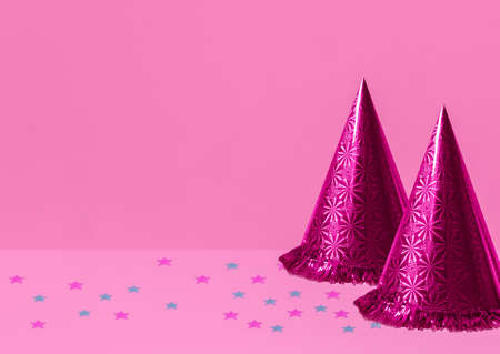 Pink party hats. Photo with copy space. Two shining cones and colorful confetti on pink backdropの写真素材