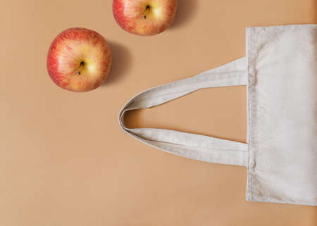 Eco bag. Top view photo with copy space. White tote bag and fresh red apples on beige backdropの写真素材