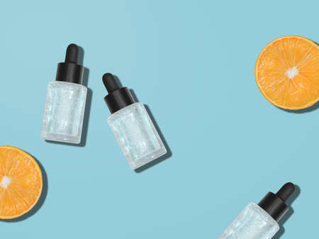 Serum. top view photo. Glass cosmetic bottles and oranges on blue background