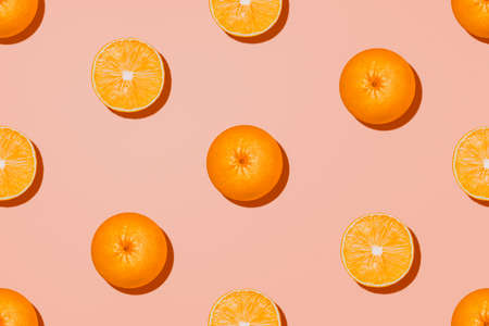 Orange fruit top view. Halves and whole oranges on pastel pink background