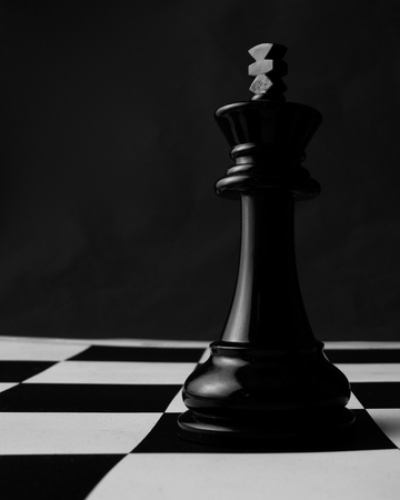 A black king chess piece stands alone on the chess board.の写真素材