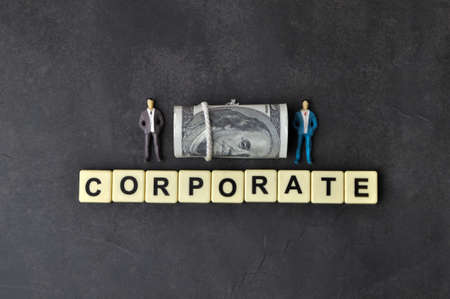 Top view of people miniatures, money banknote and square letters with text CORPORATE.の写真素材