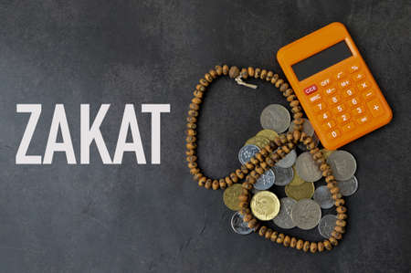 Top view of calculator, prayer beads and coins over black background written with ZAKATの写真素材