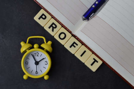 Top view of clock, pen, notebook and square letters with text PROFIT.の写真素材