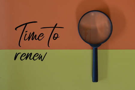Top view of magnifying glass over yellow and orange background with text TIME TO RENEW.の写真素材