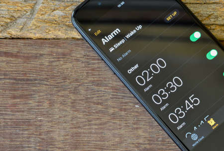 Klang,Malaysia: February 13, 2021- Alarm clock on smartphone screen over wooden background.のeditorial素材
