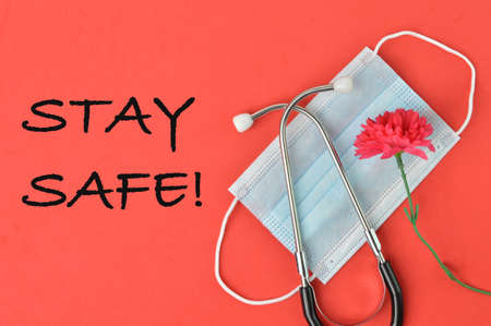 Top view of flower, stethoscope and face mask over red background written with STAY SAFE!の写真素材