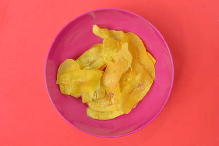 Banana slice chips in a purple bowl over red background.