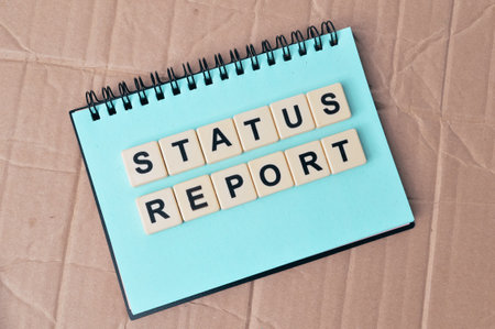 Top view of notebook and square letters with text STATUS REPORT.