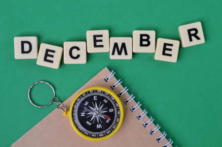 Top view of magnetic compass, notebook and square letters with text DECEMBER