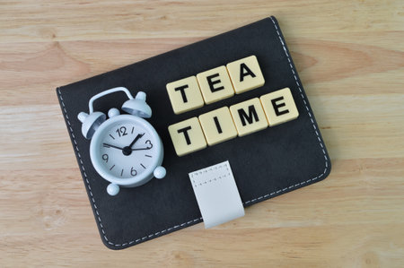 Top view of clock, notebook and block letters with text TEA TIME over wooden background.