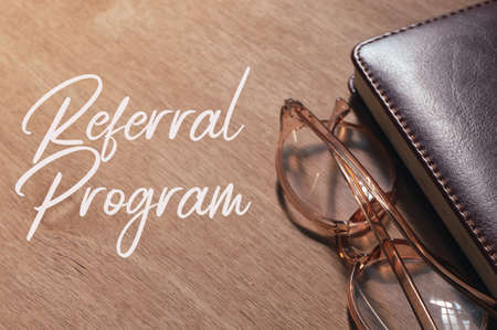 Top angle view of notebook and eyeglasses on wooden board written with REFERRAL PROGRAMの写真素材