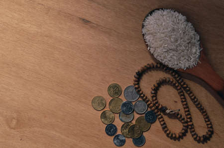 Top view of rice on wooden spoon, prayer beads and coins over wooden background. Zakat concept.の写真素材
