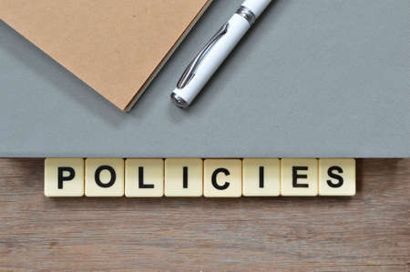 Top view of notebooks, pen and square letters with text POLICIES.の写真素材