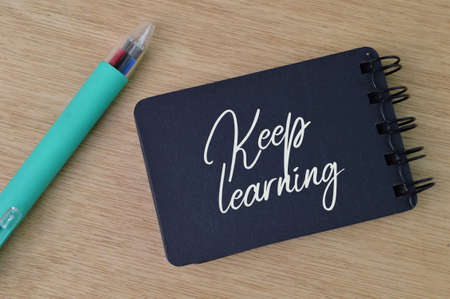 Pen and notebook written with text KEEP LEARNING.