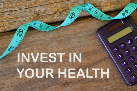 Measuring tape and calculator over wooden background written with text INVEST IN YOUR HEALTH.の写真素材