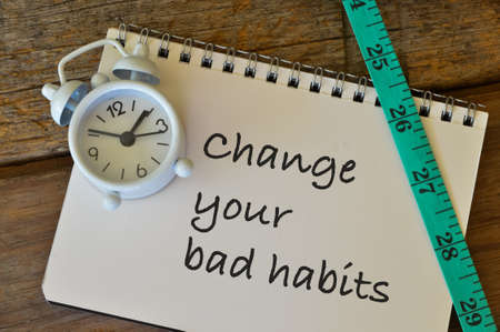Top view of clock, measuring tape and notebook written with CHANGE YOUR BAD HABITS.