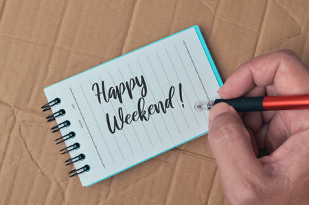 Notebook written with text HAPPY WEEKEND! over cork board background.の写真素材