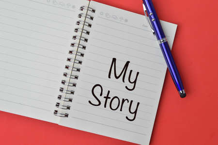 Pen and notebook written with text MY STORY over red background.の写真素材