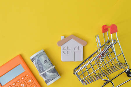 Calculator, toy house, money banknote and shopping cart over yellow background with copy space.の写真素材