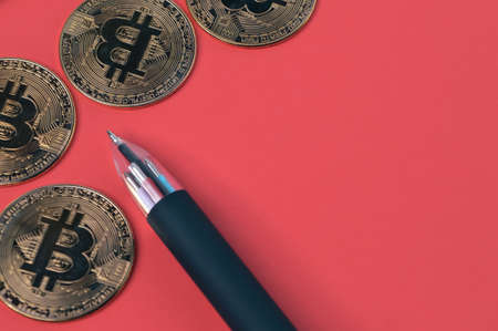Pen and golden bitcoins over red background with copy space.