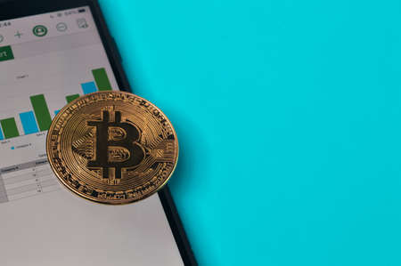 Golden bitcoin and smartphone over blue background.