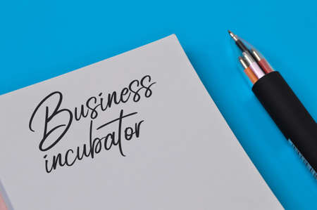 Notebook written with text BUSINESS INCUBATOR over blue background.の写真素材