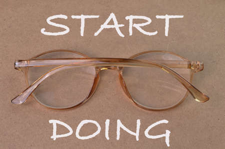 Eyeglasses over brown background written with text START DOING.
