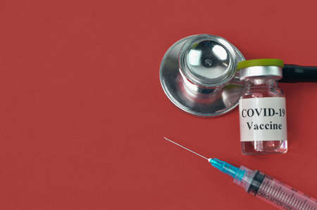 Syringe, stethoscope and Covid-19 bottle vaccination over red background.