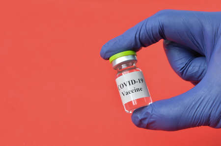Hand holding Covid-19 bottle vaccination over red background.の写真素材