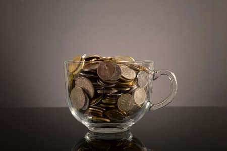 Bunch of coins in a glass cup on the table over black backgroundの写真素材
