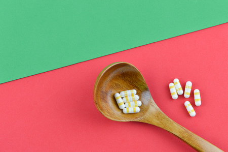 Pill capsules on wooden spoon over red and green backgroundの写真素材