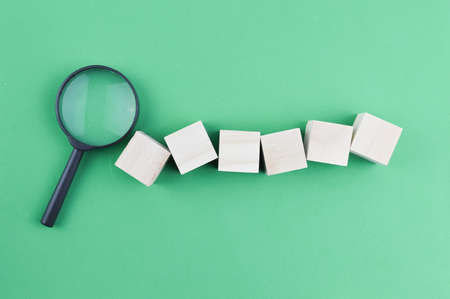 Wooden blocks and magnifying glass over green background.の写真素材