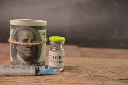 Syringe, money banknote and Coronavirus Covid-19 bottle vaccination over wooden background.の写真素材