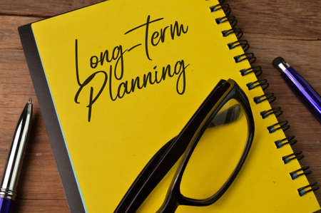 Top view of pen, eyeglasses and notebook written with LONG-TERM PLANNINGの写真素材