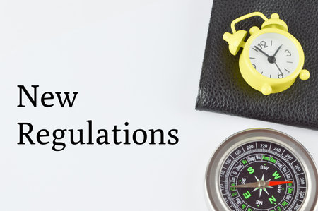 Top view of compass, clock and file over white background with text NEW REGULATIONS
