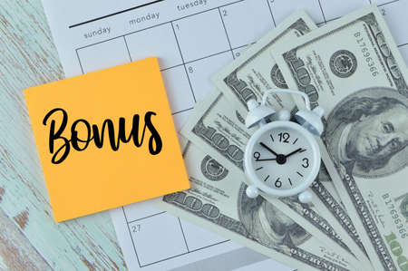 Top view of clock, money banknotes and memo note written with BONUS.の写真素材